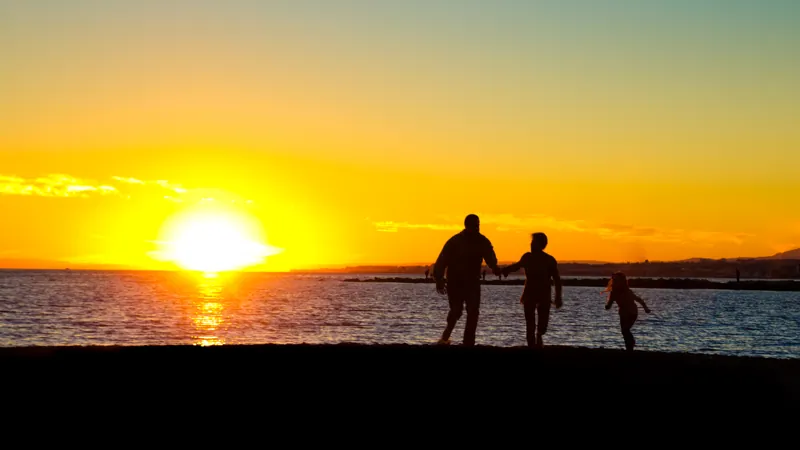 Família caminhando de mãos dadas na praia ao pôr do sol